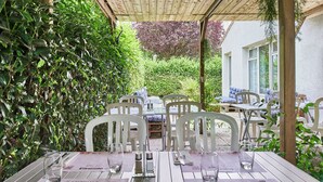 An outdoor dining area with white plastic chairs and tables, surrounded by greenery. - The Originals City, Hôtel La Verrière – Yvelines (La Verriere)