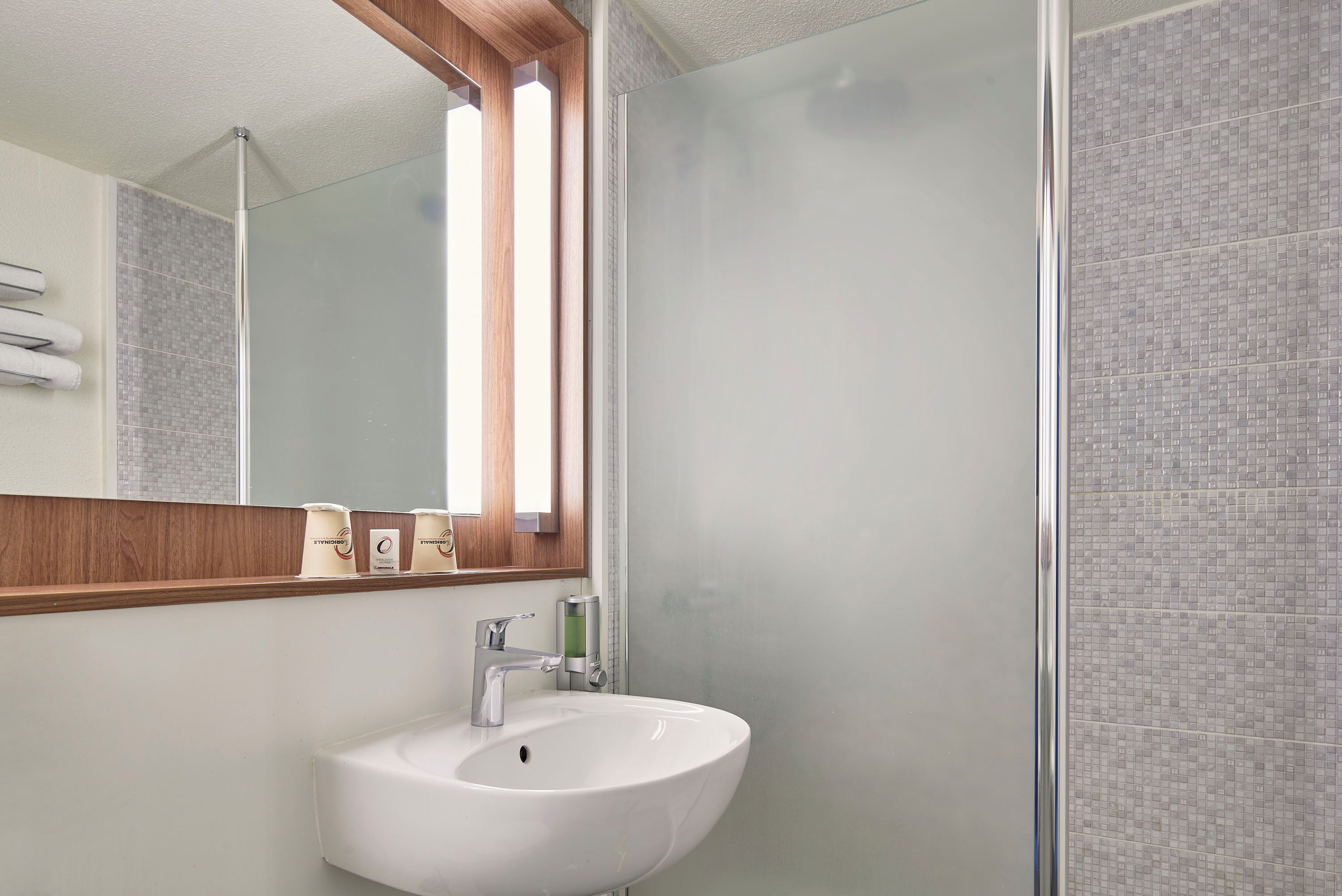 Un baño moderno con un lavamanos blanco, un espejo y zona de ducha.