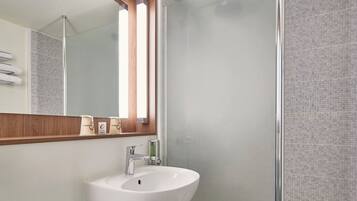 Un baño moderno con un lavamanos blanco, un espejo y zona de ducha.