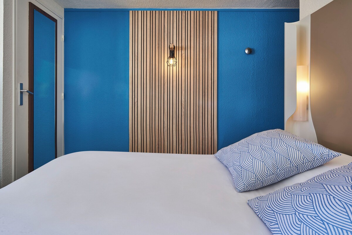 Quarto de hotel com cama, parede de painel de madeira e parede azul decorativa.