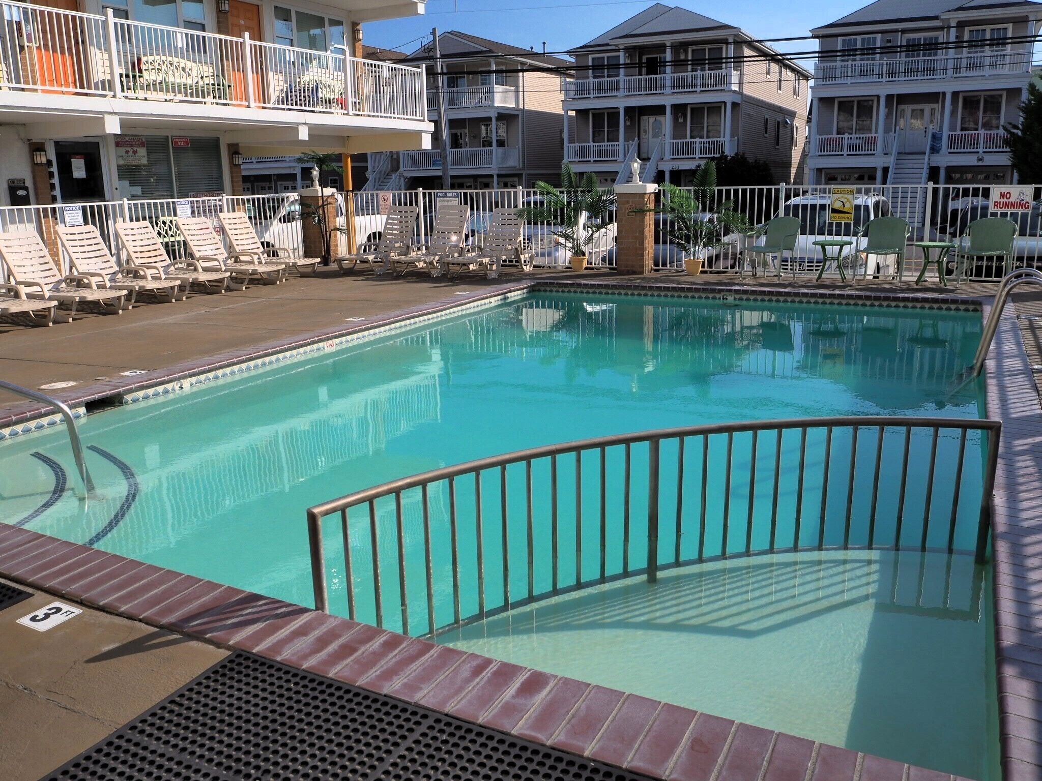 A swimming pool with a 3 ft depth marker, surrounded by lounge chairs and a fence.