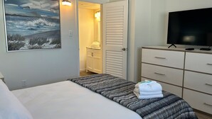 A bedroom with a bed, a television on a dresser, a painting on the wall, and a bathroom visible through an open door. - Esplanade Suites, a Sundance Vacations Property (Wildwood)