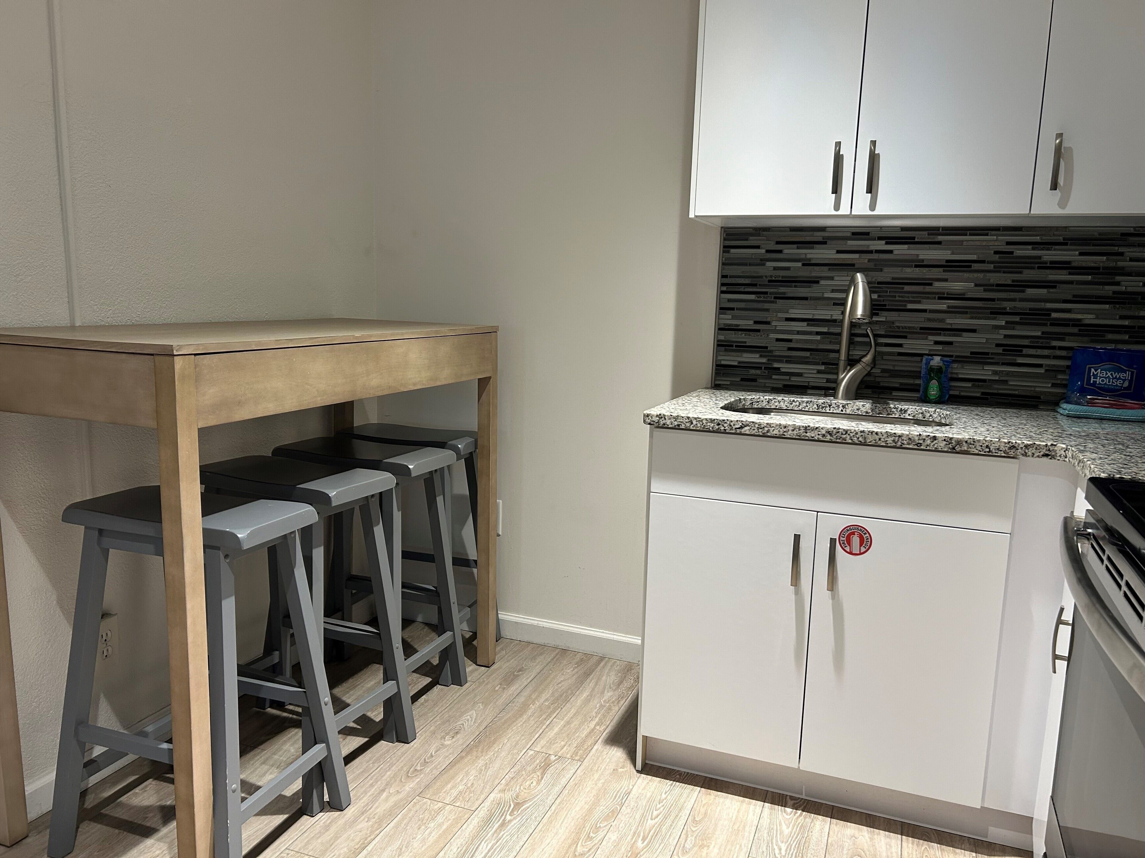 A kitchen with white cabinets, a granite countertop, and a wooden table with bar stools.