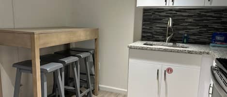 A kitchen with white cabinets, a granite countertop, and a wooden table with bar stools.