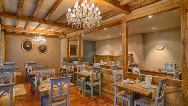 Un restaurant doté de poutres en bois, de lustres et d’une décoration rustique. Les tables et les chaises sont disposées pour accueillir les clients.