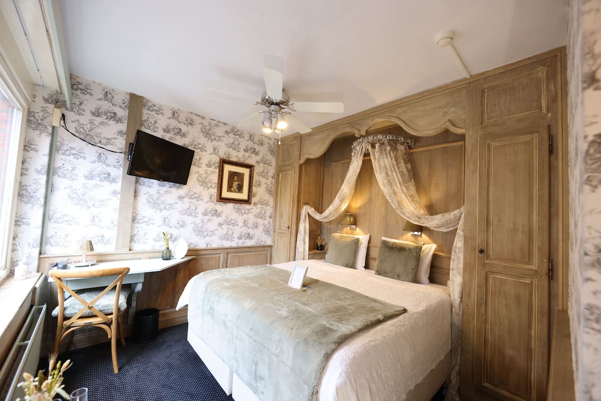 Een slaapkamer met een groot bed, een bureau, een stoel, een plafondventilator en een kledingkast.