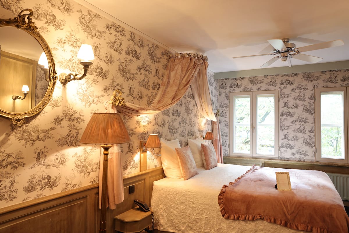 Een slaapkamer met een groot bed, een plafondventilator en bloemenbehang.