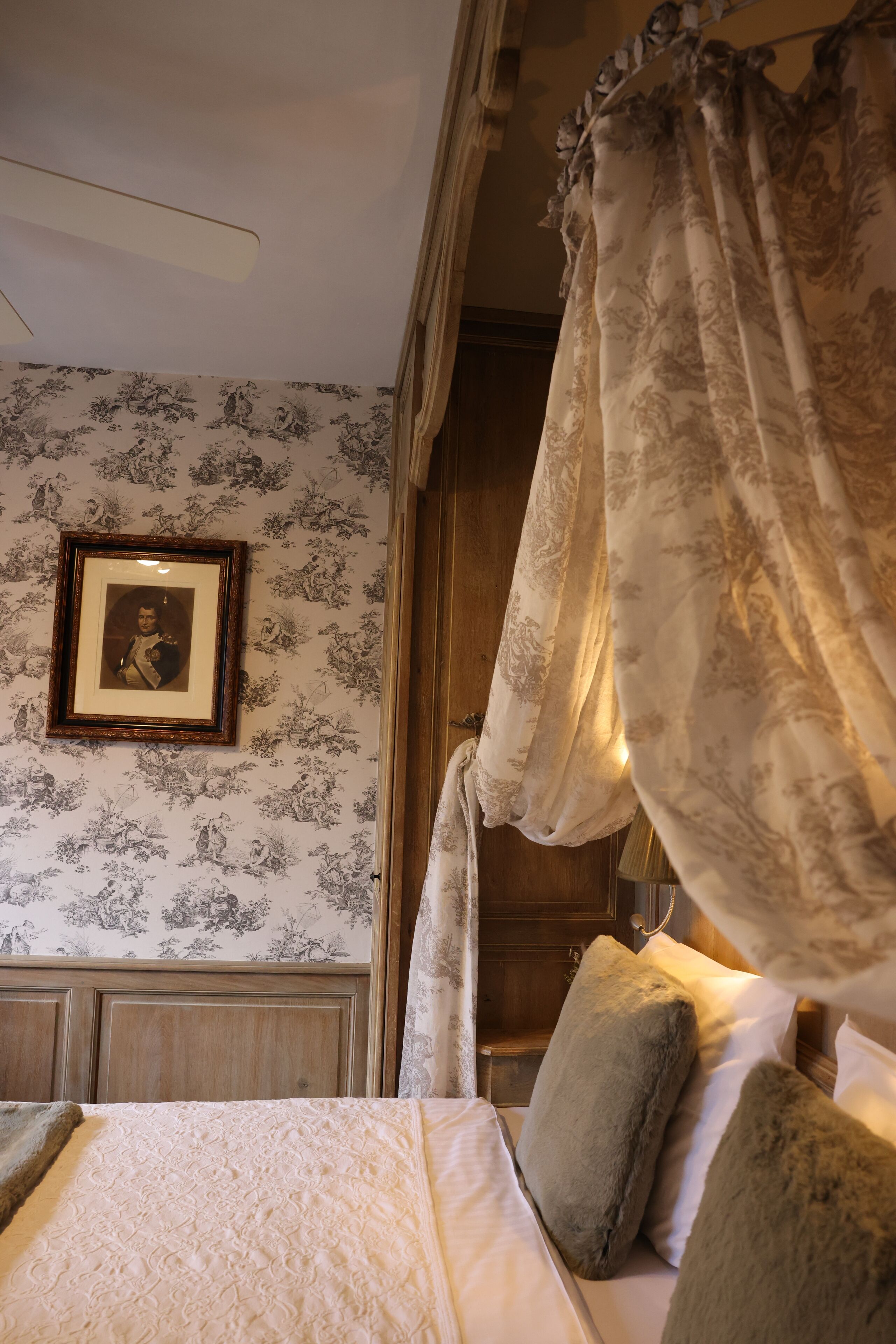 A bedroom with a canopy bed, floral wallpaper, and a framed picture on the wall.