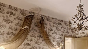 Une chambre à coucher avec une tête de lit capitonnée, un lit recouvert de draps blancs, un ours en peluche posé sur les oreillers et un lustre.