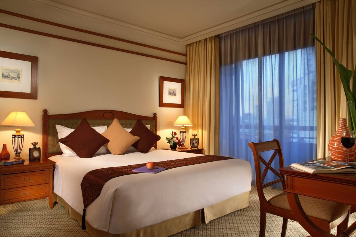 Une chambre d’hôtel avec un grand lit, deux tables de chevet avec des lampes, une chaise et une vue sur la ville par la fenêtre.