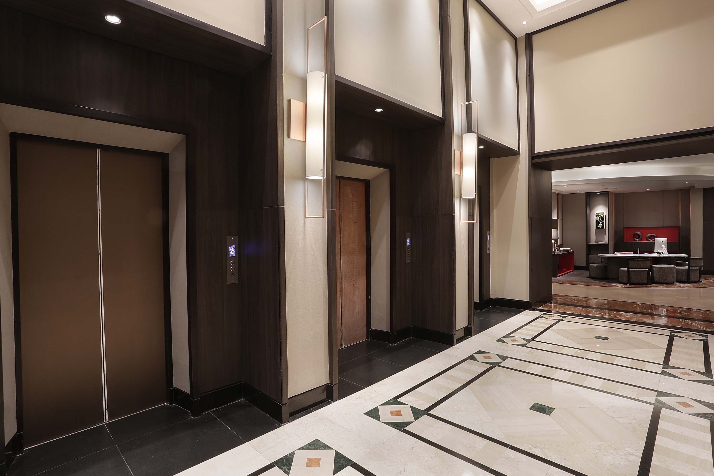 A hotel lobby with a modern design, featuring a tiled floor, wooden doors, and a seating area with a red accent wall.