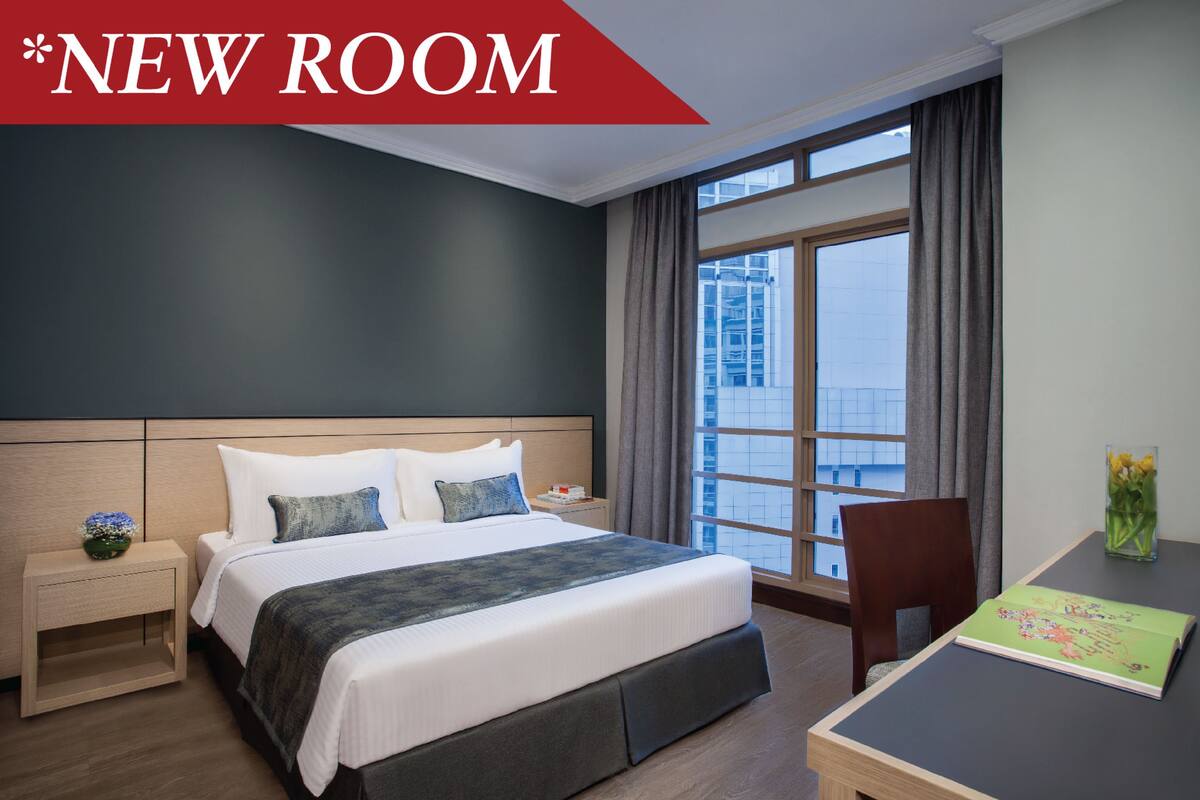 Une chambre d’hôtel avec un grand lit, une table de chevet, un bureau avec une chaise et une fenêtre avec des rideaux.