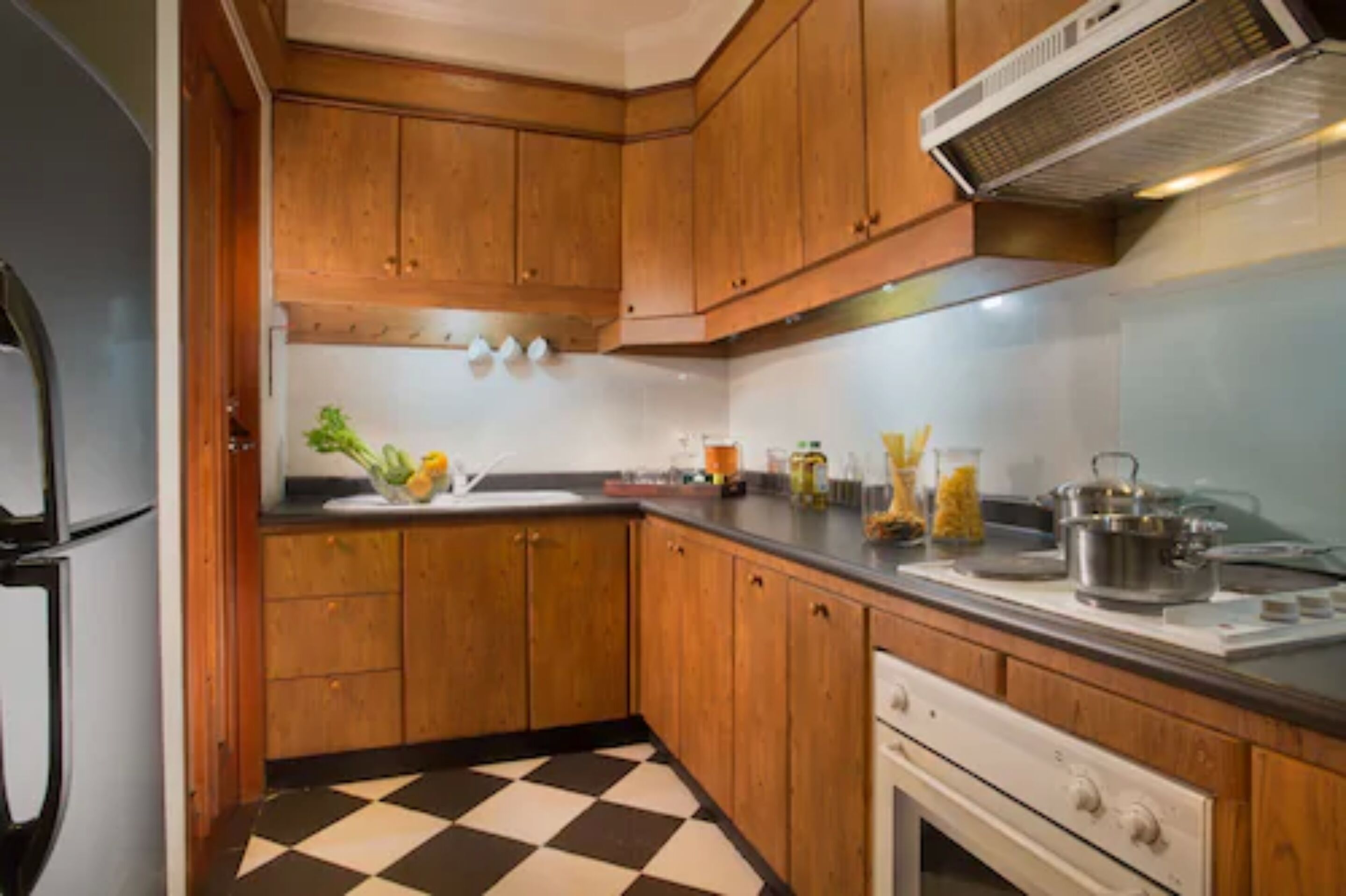 A kitchen with wooden cabinets, a black and white checkered floor, and various kitchen items on the counter.