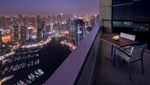 A balcony with a table and chairs overlooking a marina and city skyline at night.