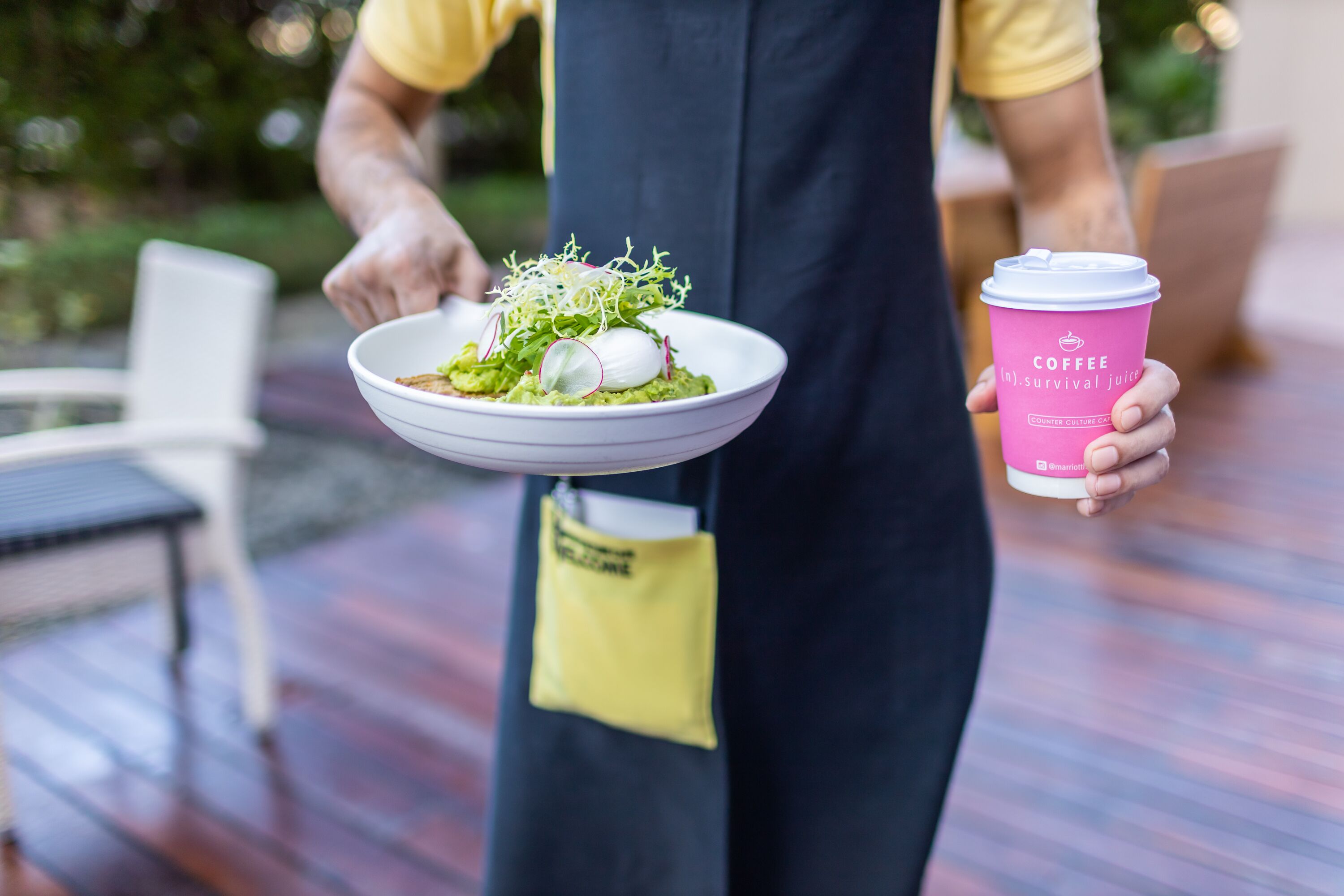 A person holding a bowl of food and a pink coffee cup with a lid.