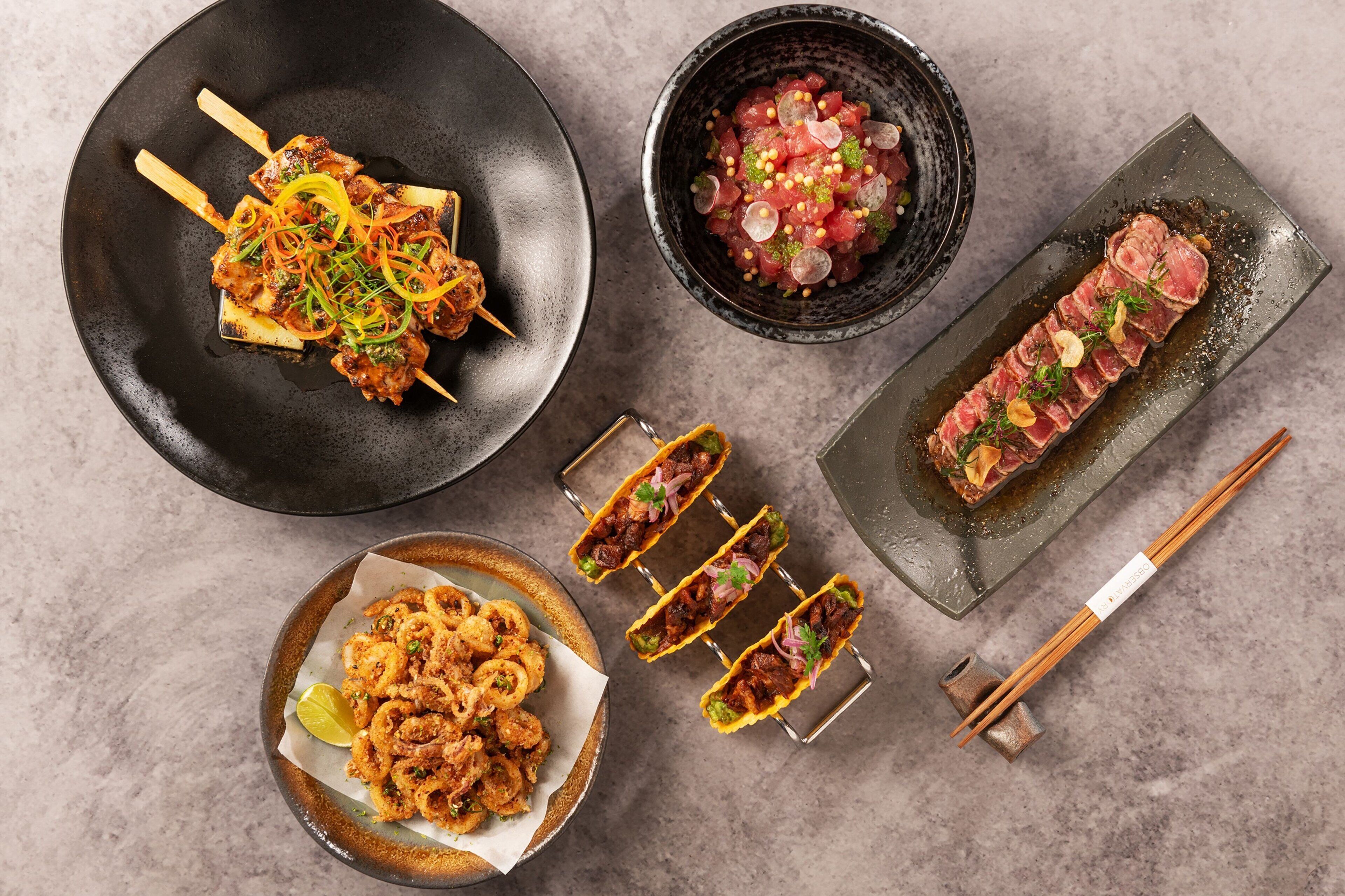 Un assortiment de plats comprenant des brochettes, des sashimis et des calamars frits.