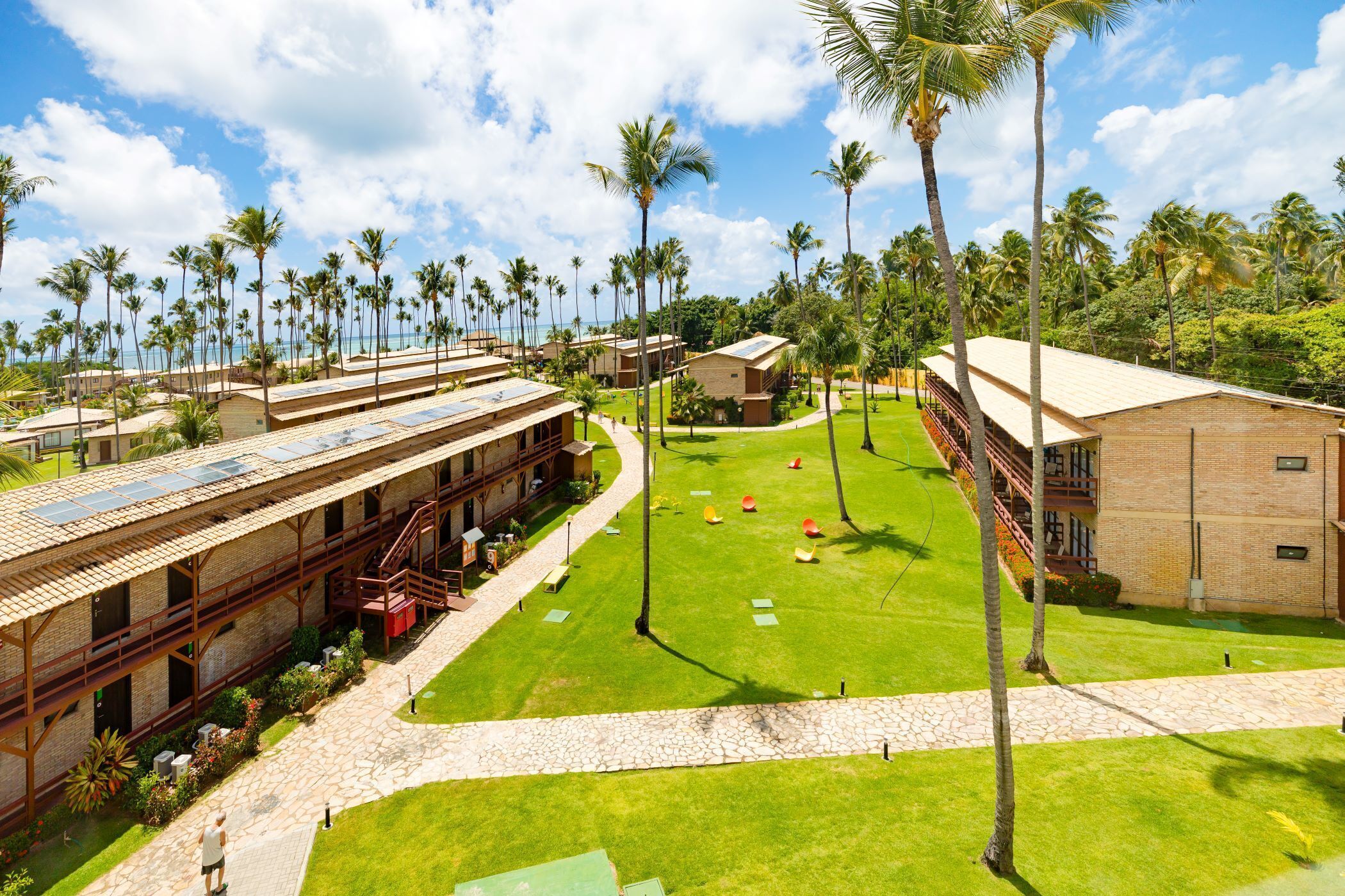 A resort with multiple buildings, a central grassy area, and palm trees.