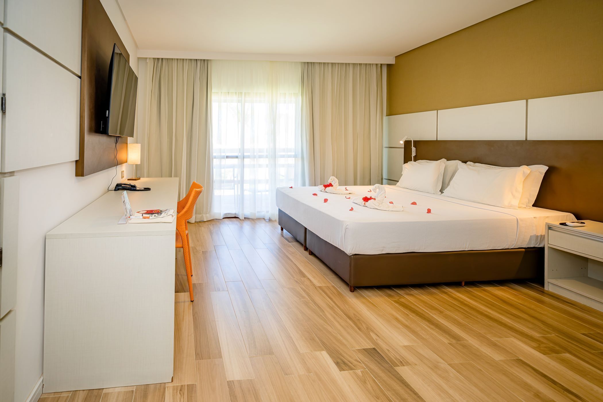 A hotel room with a bed, a desk, a chair, a TV, and a window with curtains.