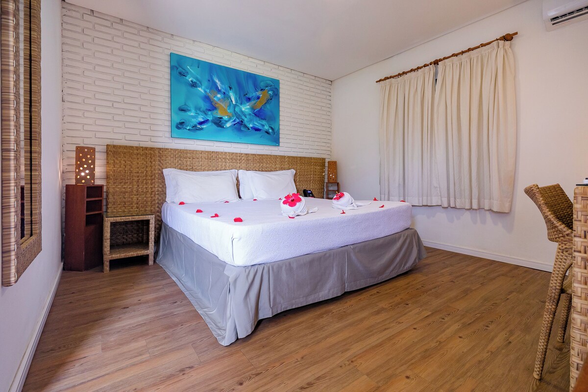 A neatly made bed with rose petals, a white brick wall, and a large abstract painting.