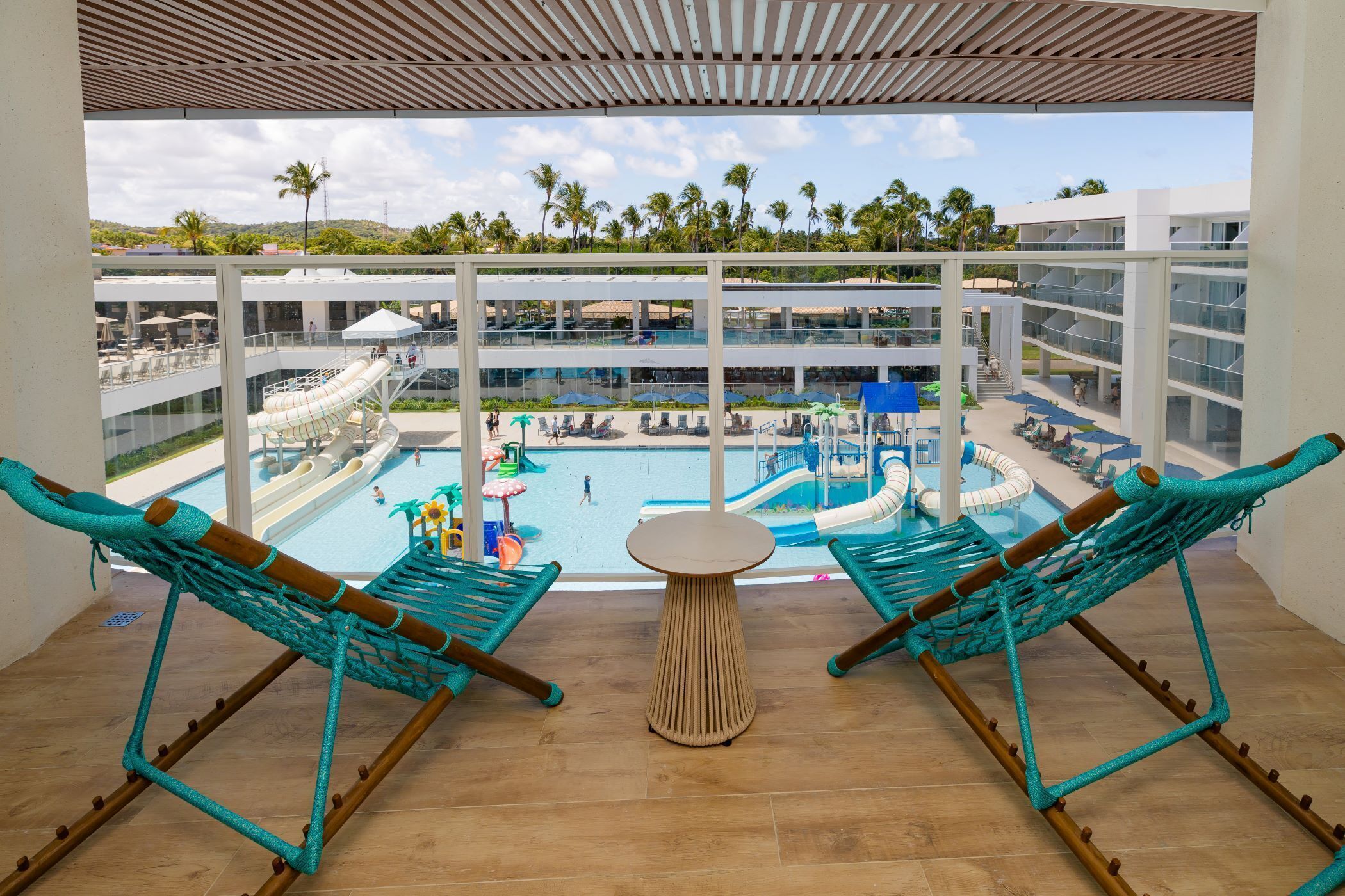 A balcony with two turquoise hammocks, a small round table, and a view of a pool area with slides and umbrellas.