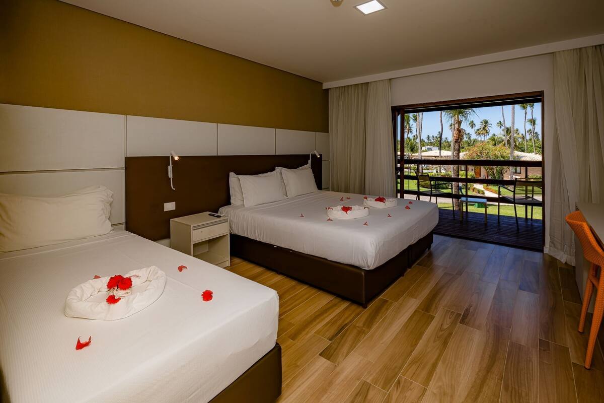 A hotel room with two beds, a balcony with a view of palm trees, and a wooden floor.