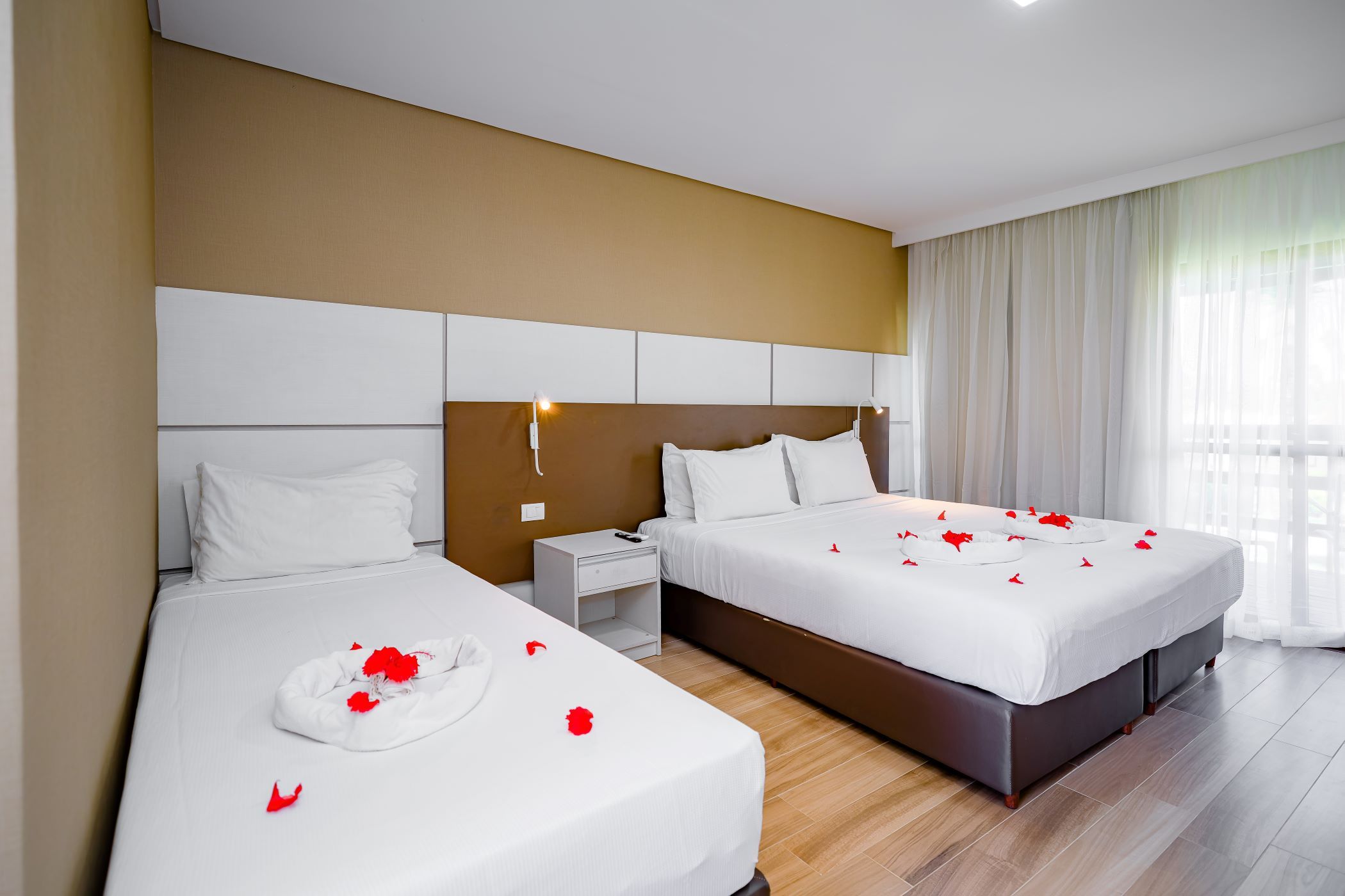 A hotel room with two beds, a nightstand, a wall-mounted phone, and a window with curtains.