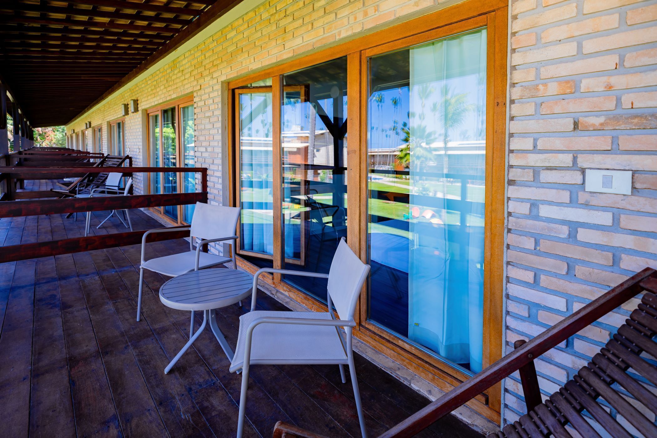 A covered outdoor seating area with metal chairs and tables, a brick wall, and large glass doors.