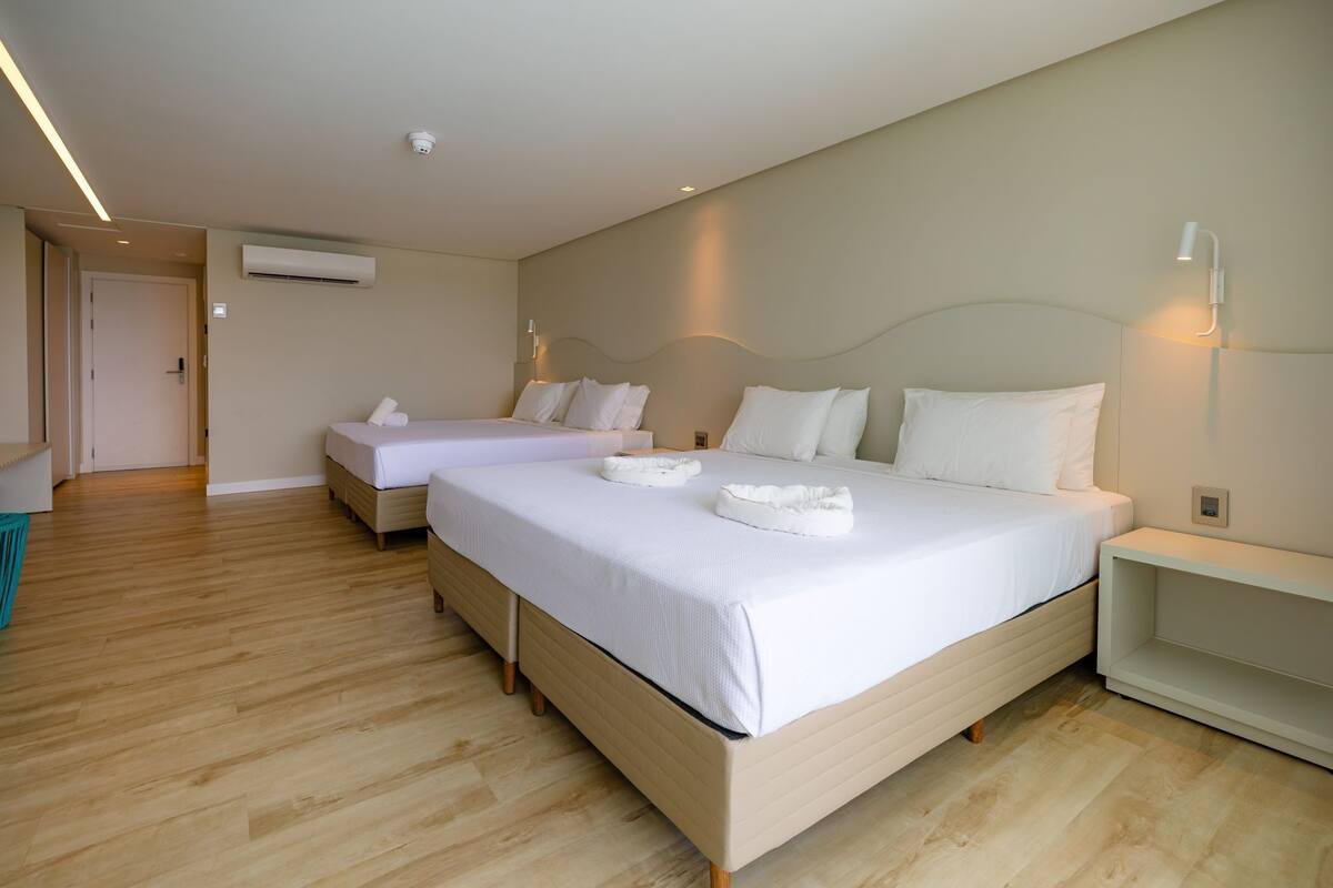 A hotel room with two beds, a wooden floor, a white wall, and a ceiling-mounted air conditioner.