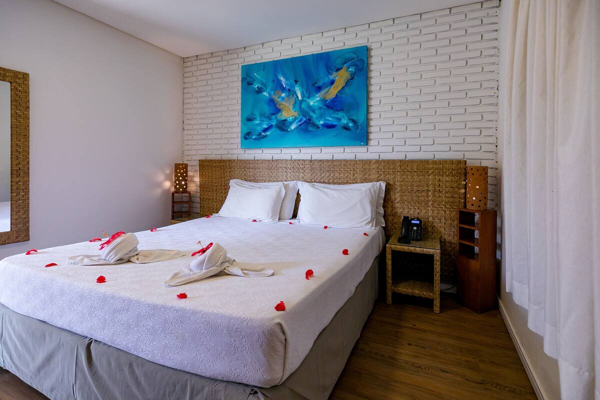 A hotel room with a large bed, white linens, a blue abstract painting on the wall, and a wooden headboard.
