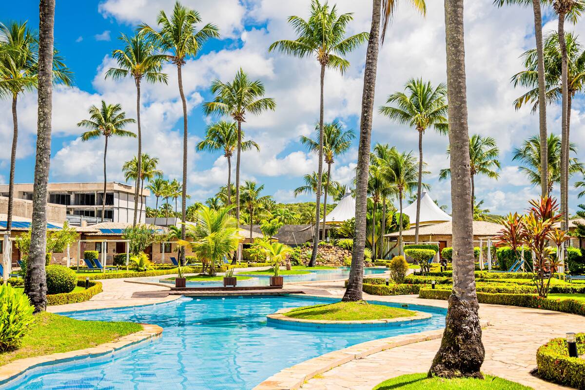 A resort with a swimming pool, palm trees, and a building with a white roof.