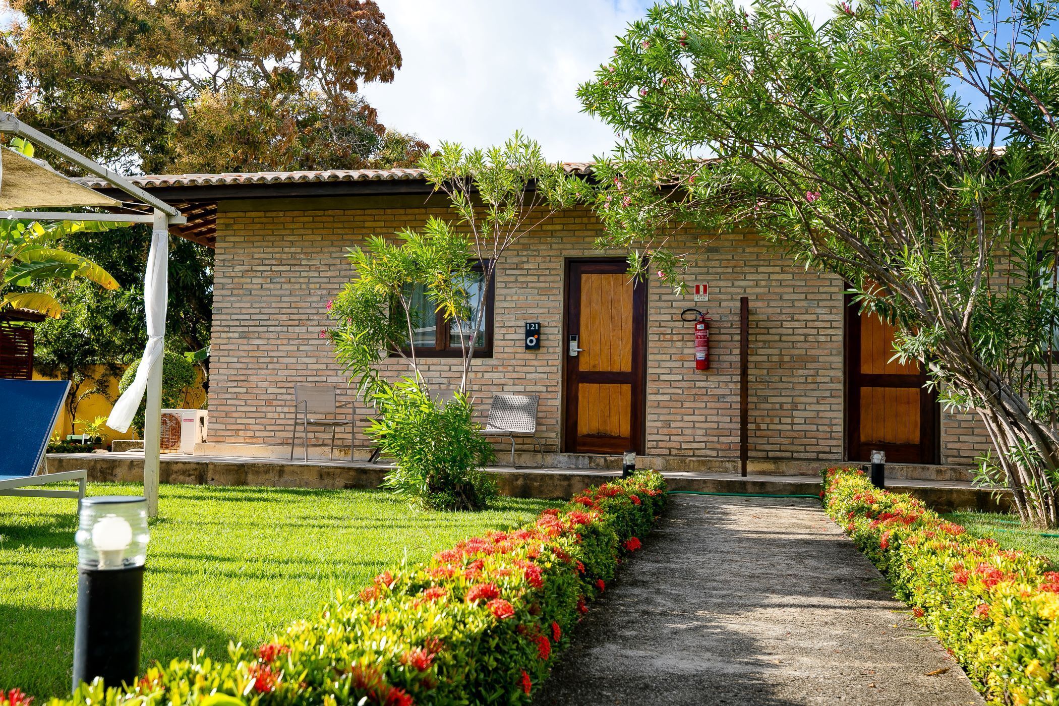 A brick building with a paved pathway leading to a wooden door, surrounded by well-maintained gardens and a clear sky.