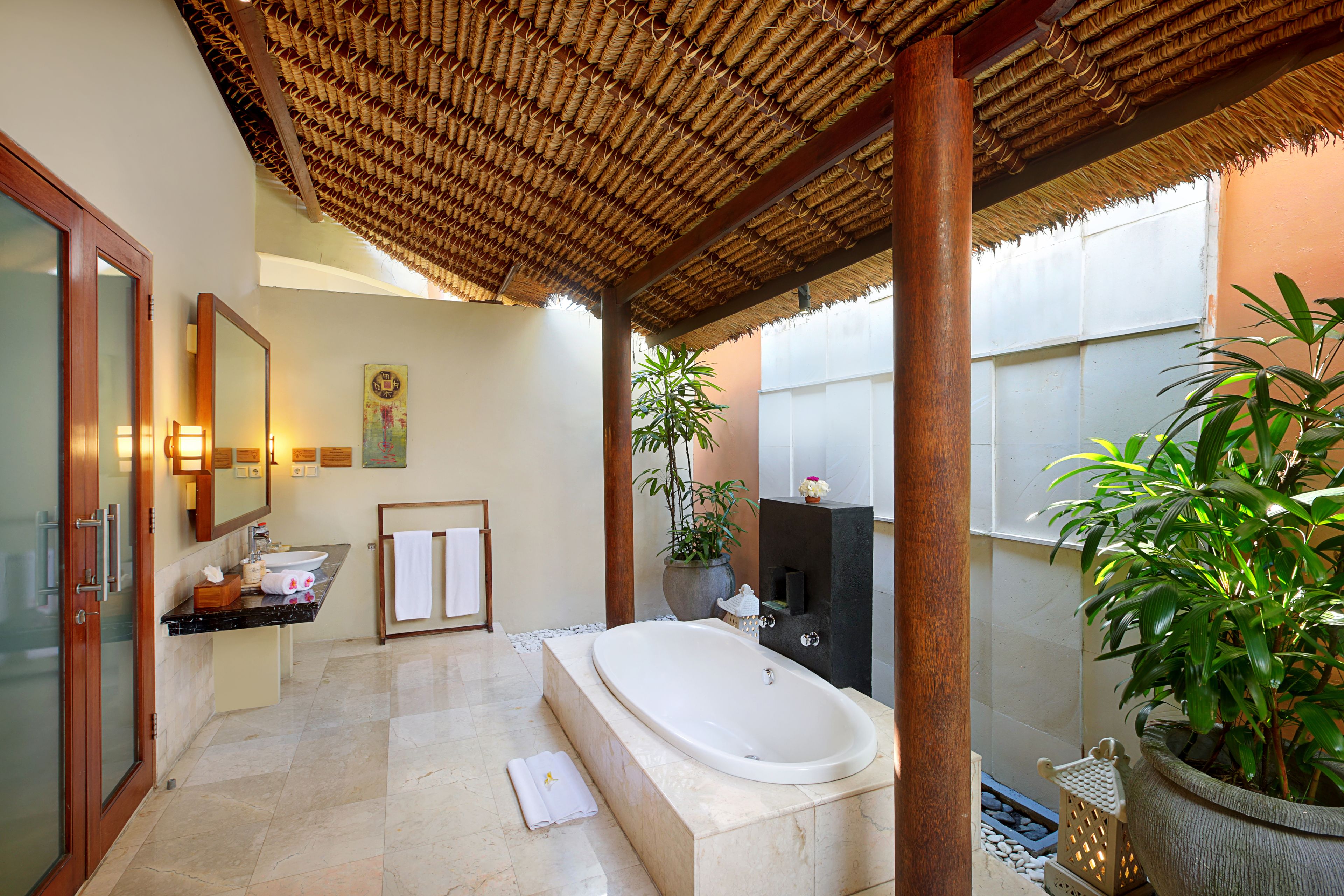 A bathroom with a large bathtub, a sink, a mirror, and a potted plant.