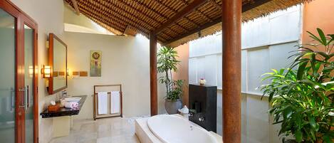 A bathroom with a large bathtub, a sink, a mirror, and a potted plant.