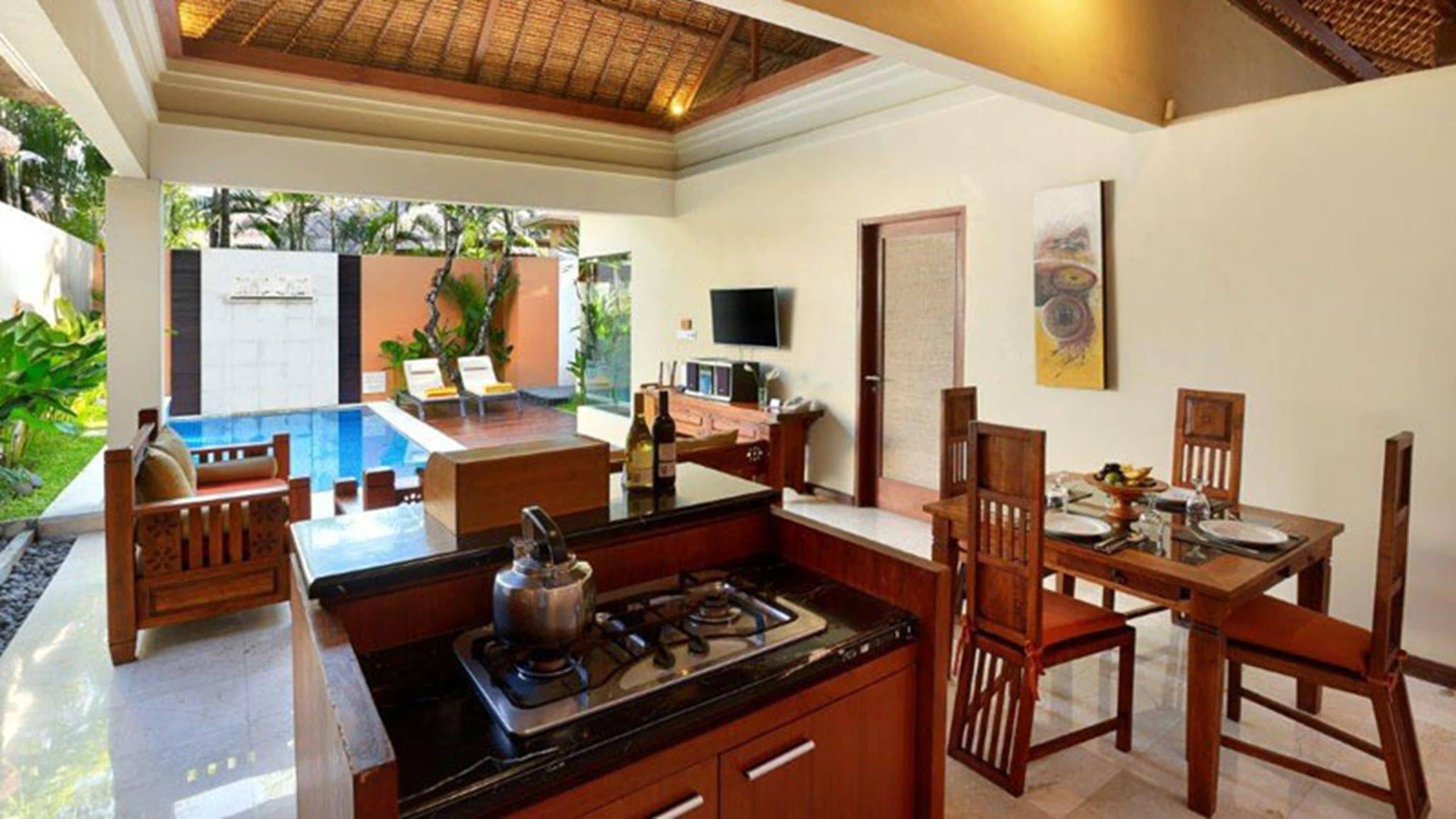 A kitchen with a gas stove, a sink, and a dining area with wooden chairs and a table.
