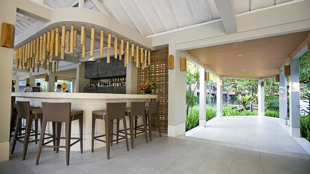 A modern bar area with wicker bar stools, a curved ceiling, and a view of a lush garden. - Dewi Sri Hotel (Kuta)
