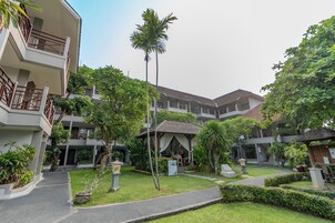 A multi-story hotel with a central courtyard, surrounded by lush greenery and palm trees.