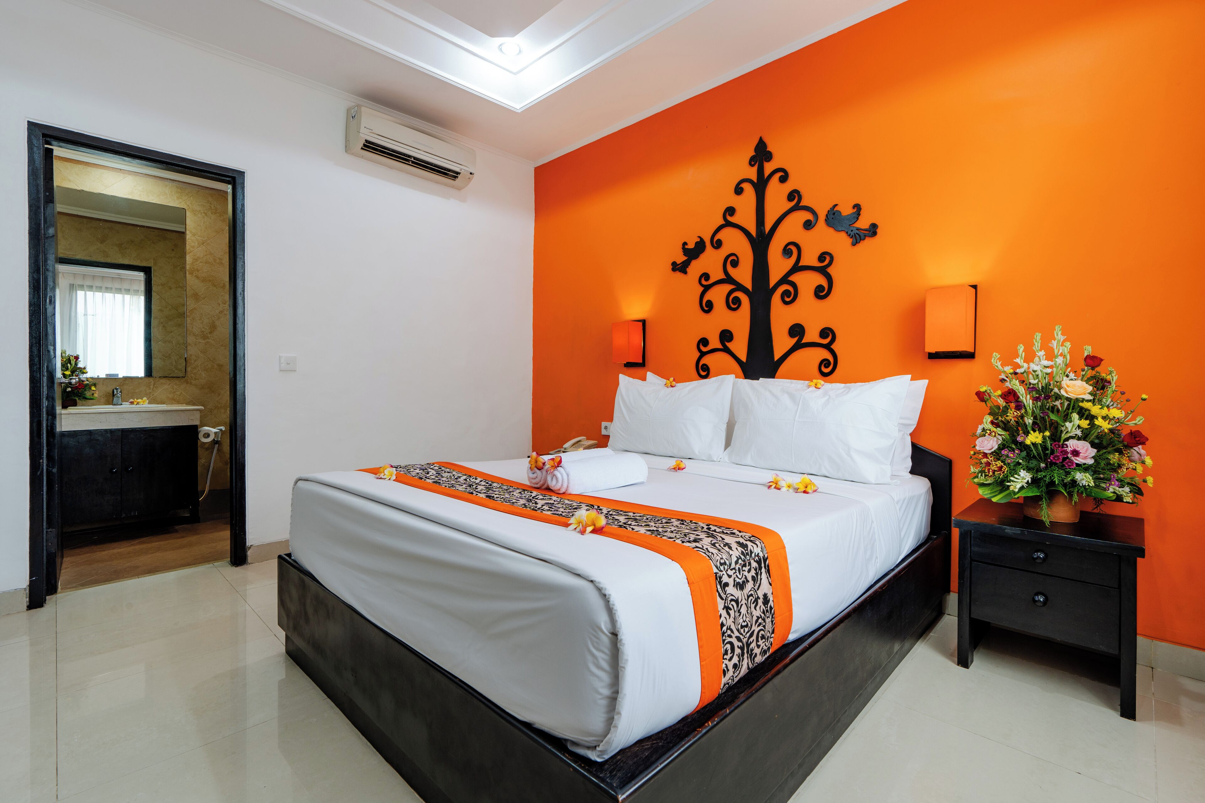 Quarto de hotel com cama, mesa de cabeceira, espelho e banheiro visível por uma porta aberta.