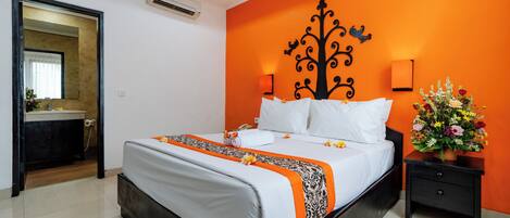 Quarto de hotel com cama, mesa de cabeceira, espelho e banheiro visível por uma porta aberta.