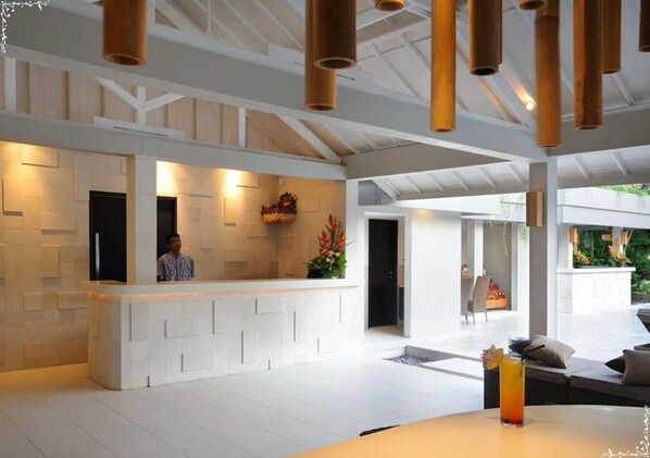 Un hall d’entrée spacieux comprenant un comptoir d’accueil, un espace détente avec une table et des chaises, et une vue sur l’extérieur.