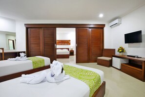 A hotel room with two beds, a TV, a desk, and a wardrobe. - Dewi Sri Hotel (Kuta)