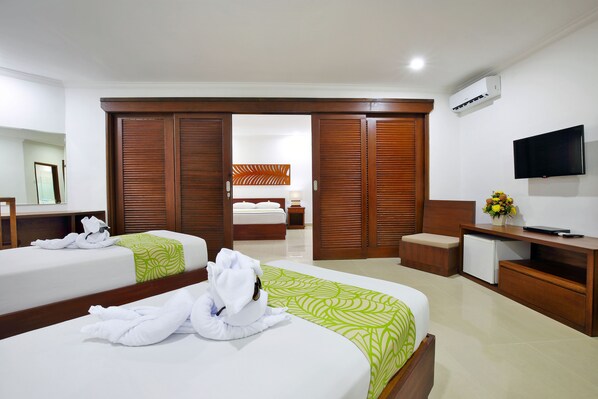 A hotel room with two beds, a TV, a desk, and a wardrobe. - Dewi Sri Hotel (Kuta)