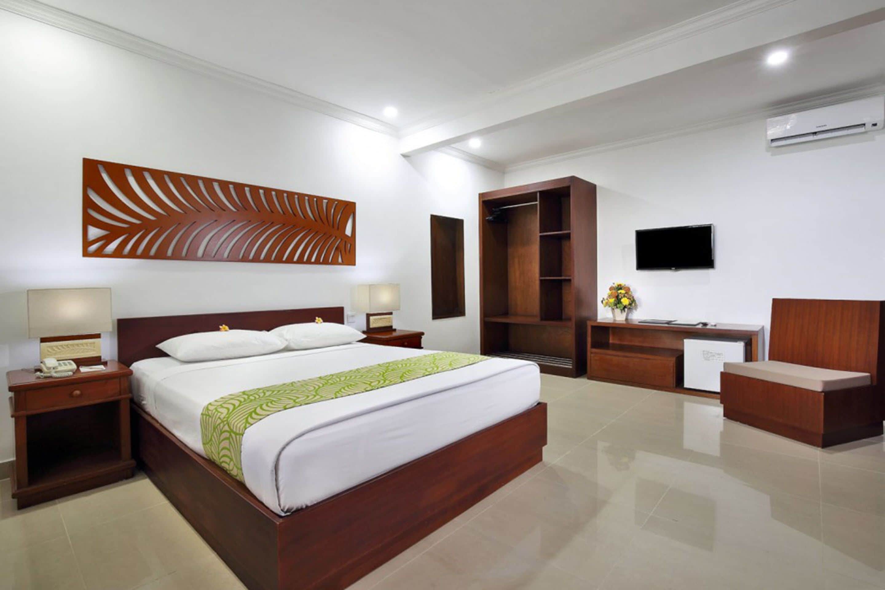 Une chambre d’hôtel moderne dotée d’un grand lit, d’une tête de lit en bois, de tables de chevet, d’un bureau, d’une armoire et d’un téléviseur à écran plat.