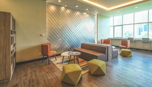 A modern lounge area with a herringbone-patterned wall, a sofa, two armchairs, a small table, and a yellow ottoman. - Somerset Millennium Makati (Makati)