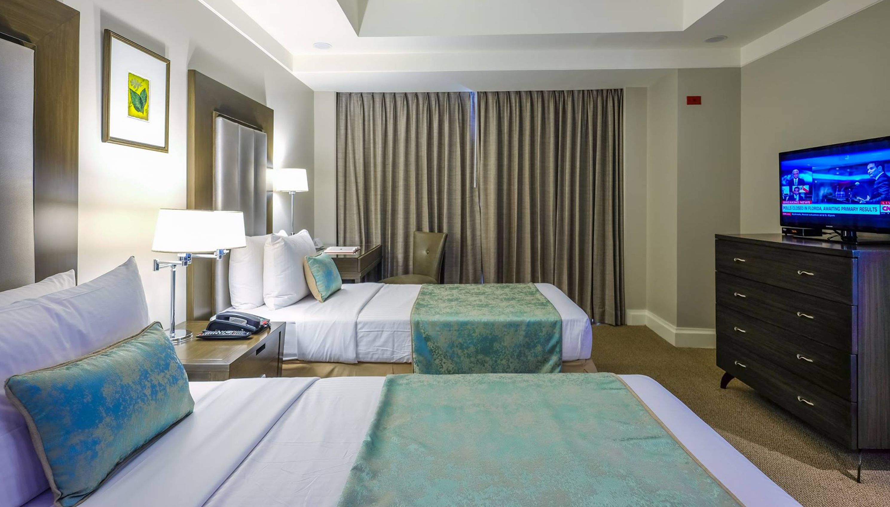 A hotel room with two beds, a television, a desk with a lamp, and a chair.