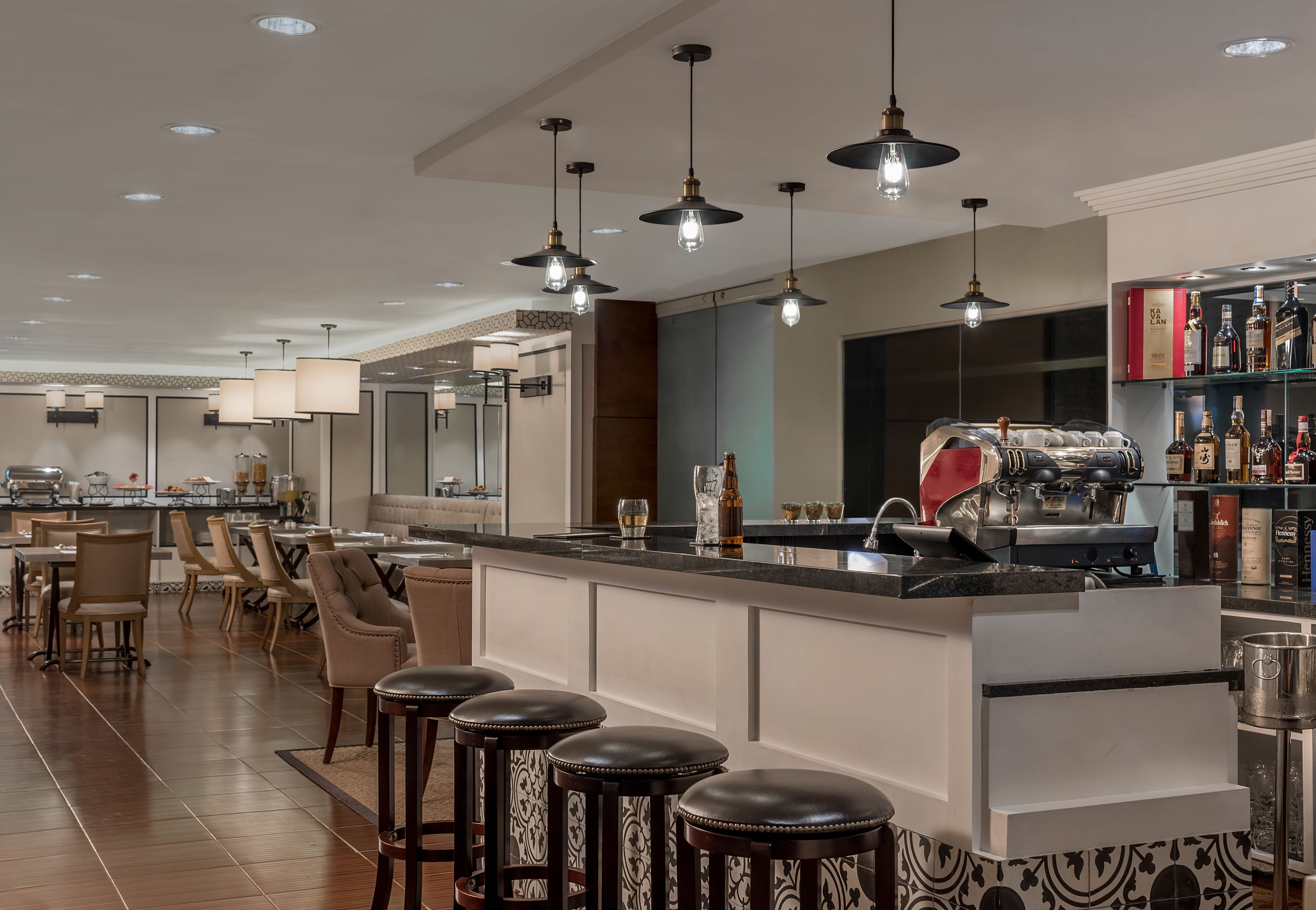 Un espace bar moderne doté d’un long comptoir, de nombreux tabourets et de luminaires suspendus.