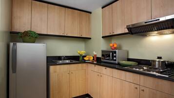 A kitchen with wooden cabinets, a stainless steel refrigerator, a microwave, a stove, and a sink.