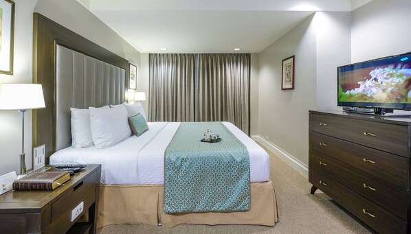 A hotel room with a large bed, a TV, a desk with a lamp, and a dresser.