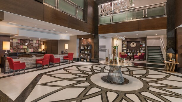 A spacious lobby with a central round table, red seating, a reception desk, and a staircase leading to an upper level. - Somerset Millennium Makati (Makati)
