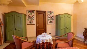 Una habitación con dos armarios verdes, una silla de madera, una mesa redonda con mantel de encaje y un sofá estampado.
