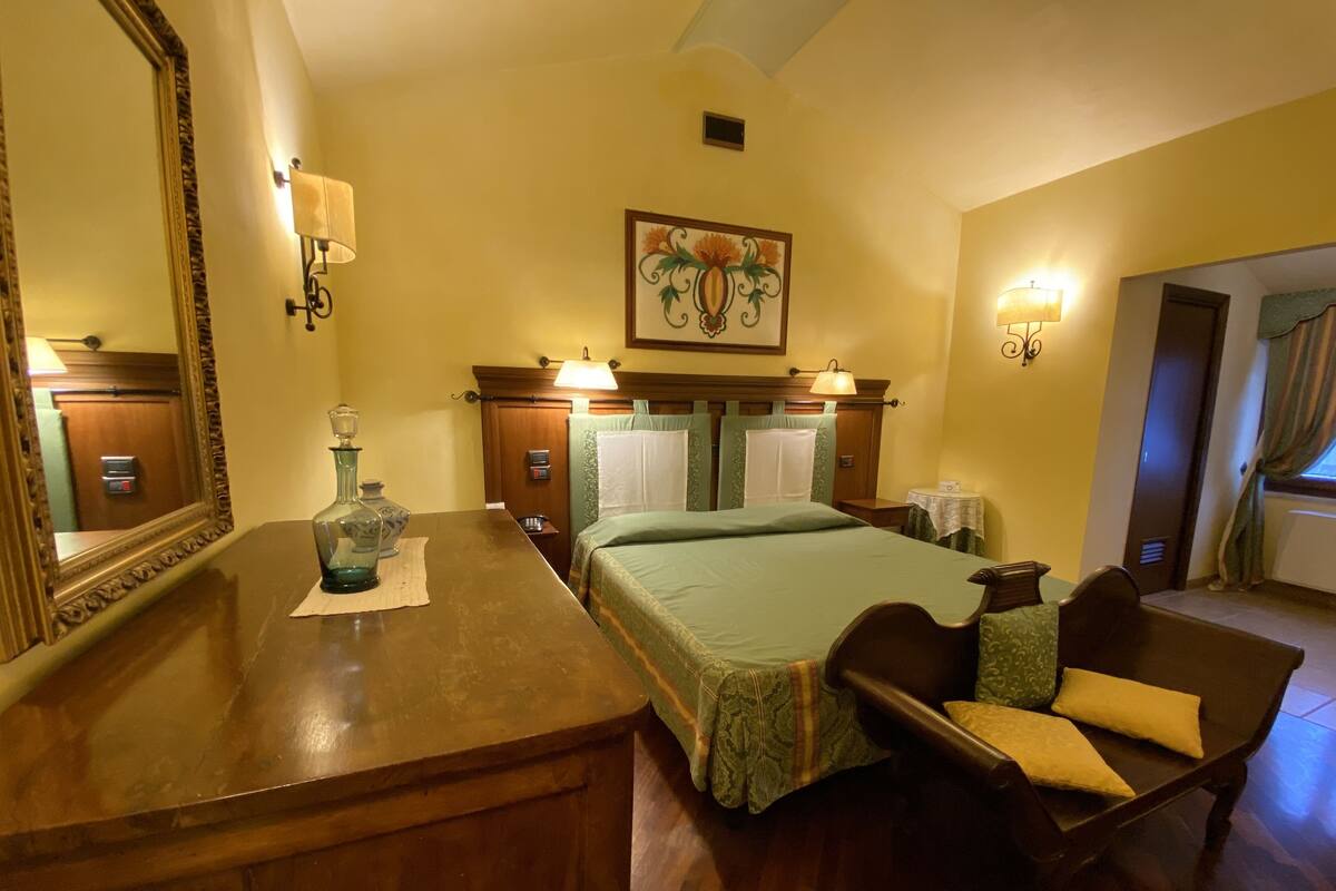 A hotel room with a wooden bed, a nightstand, a mirror, and a painting on the wall.